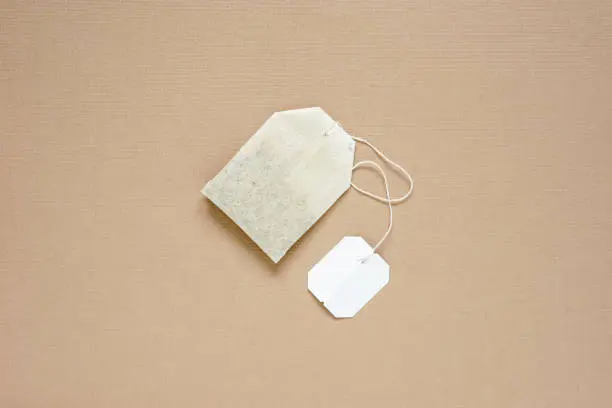 top view of dried tea bag with blank white paper tag placed on brown paper, copy space concept.