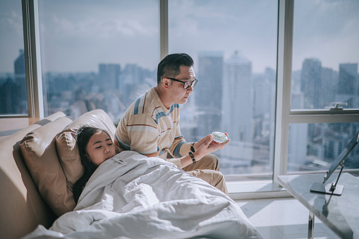asian chinesse father talking to doctor via digital tablet for his sick daughter on sofa living room videocall with his doctor via digital tablet