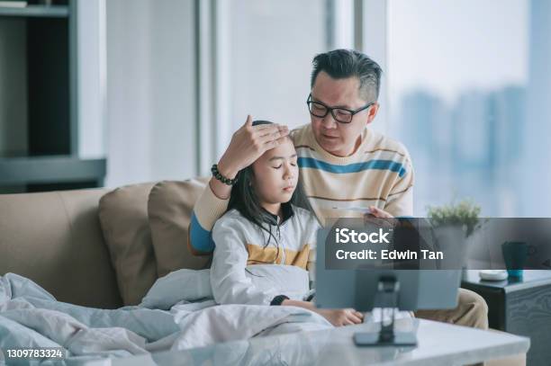 Asian Chinesse Father Taking Temperature For His Sick Daughter On Sofa Living Room Videocall With His Doctor Via Digital Tablet Stock Photo - Download Image Now