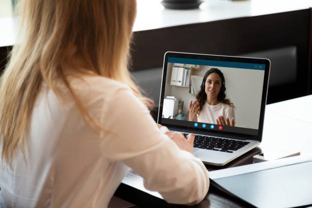 Young woman holding video call conversation with female colleague. Rear back view young woman holding video call conversation with female colleague in wireless headphones, discussing working issues remotely or taking educational online class, self-isolation concept. zoom classroom stock pictures, royalty-free photos & images