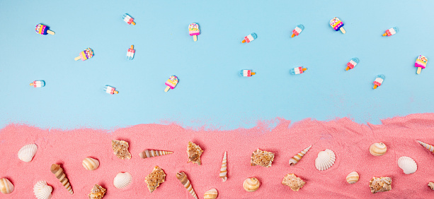 Seashells and ice creams on blue background with pink sand. Flat lay concept.