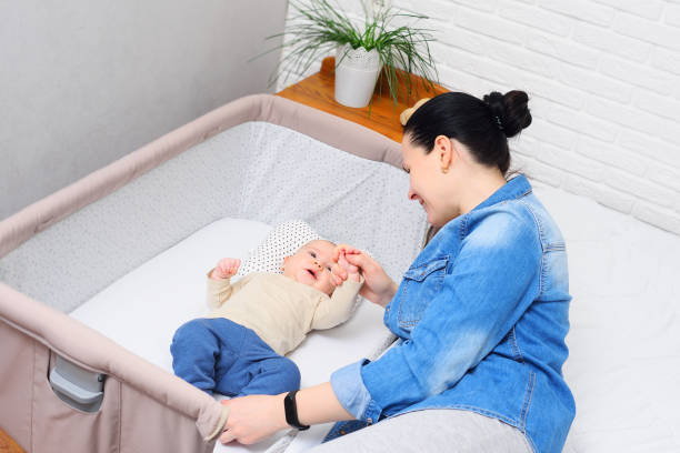 moeder speelt met een baby die in een zijbed ligt voor een pasgeborene of in een moderne box - babybox stockfoto's en -beelden