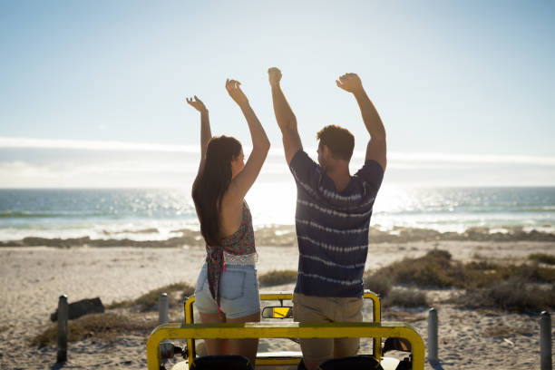 手を上げて海のそばのビーチバギーで幸せな白人カップル - beach buggy ストックフォトと画像