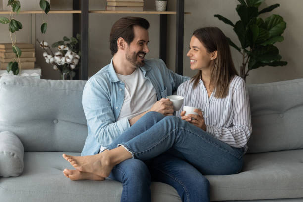istock Happy couple relaxing on couch, holding cups, drinking hot beverages 1309791009