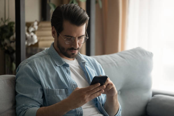 istock Close up serious man wearing glasses using smartphone at home 1309791044