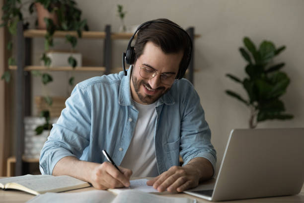 istock Close up smiling man wearing headphones taking notes, studying online 1309791164
