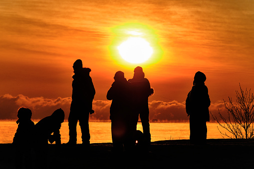 Silhouettes of people on the background of an orange sunset over the sea