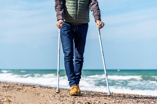 Disabled adult man using aluminum forearm crutches by the sea Stylishly dressed disabled adult man using aluminum forearm crutches as a mobility aid to walk on the seaside in Turkey. Half length view. aids walk stock pictures, royalty-free photos & images