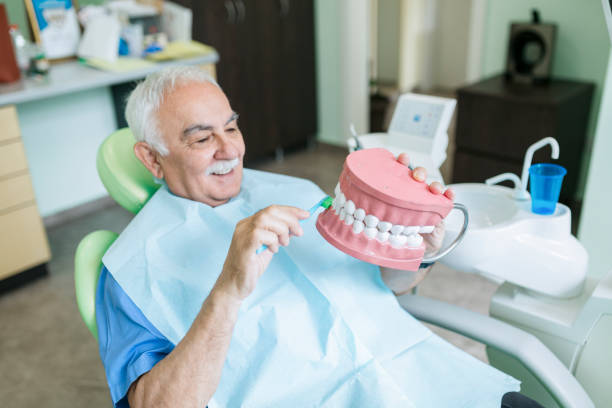 Visiting the dentist Senior Caucasian male visiting a dentist and sitting in the dentist chair, smiling and simulating brushing of teeth with a tooth brush and a big teeth prop brushing teeth stock pictures, royalty-free photos & images