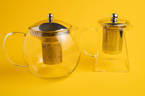 istock Different size transparent teapots on yellow background. Different glass teapot with tea strainer 1309795826