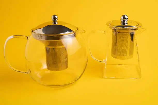 Different size transparent teapots on yellow background. Different glass teapot with tea strainer. High quality photo