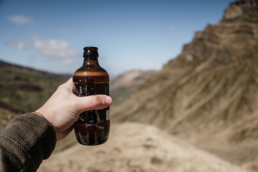 A hand in a natural area holding a beer glass bottle
