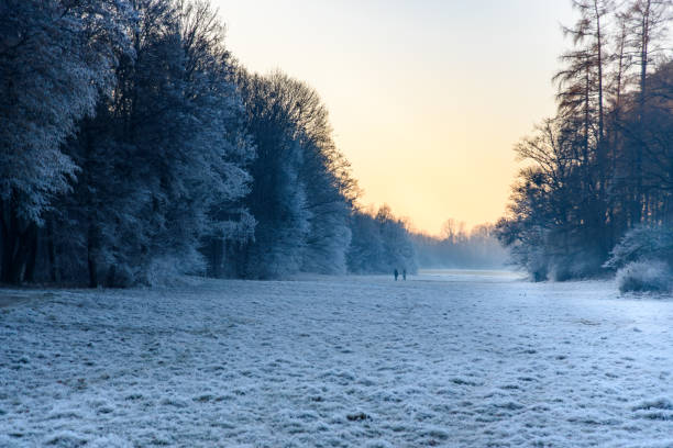 In the distance, two passers-by are talking on a frosted meadow in Munich, Germany