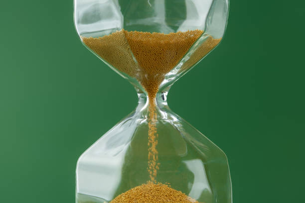 istock Gold hourglass on dark green paper background 1309796265