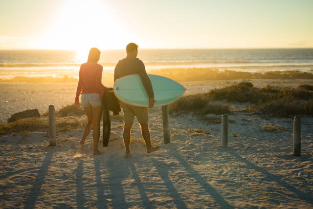 istock Caucasian couple on the beach carrying surfboard during sunset 1309800195