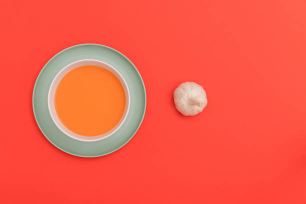 istock Gazpacho bowl on a blue plate and garlic on red background. 1309800372