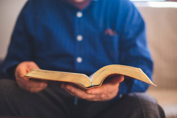 istock Elderly man sitting on couch and reading Bible 1309800434