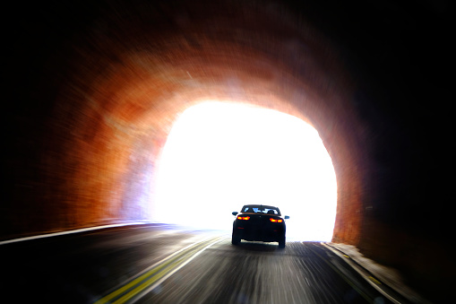 Car driving through dark tunnel and entering light of freedom