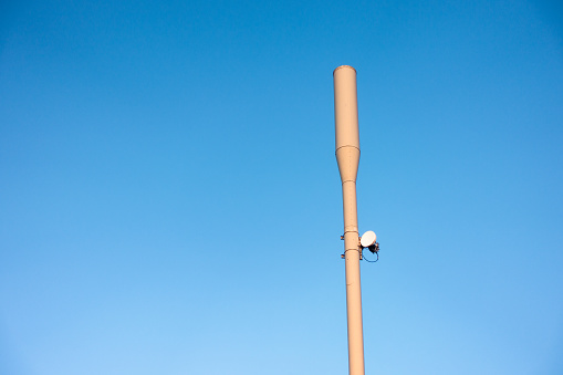 A modern, compact mobile phone antennae in an urban pole, seen against clear blue sky.