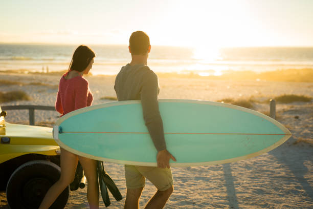 istock Caucasian couple on the beach carrying surfboard during sunset 1309801689