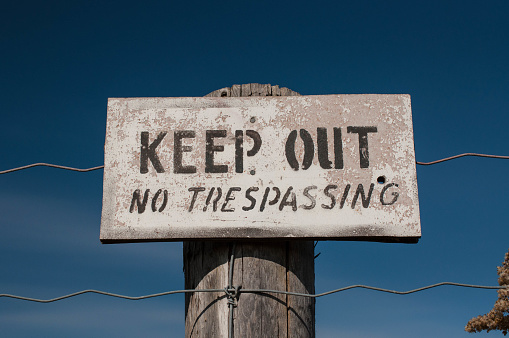 A faded warning sign reading Keep Out No Trespassing on an old wooden post with blue sky in the background