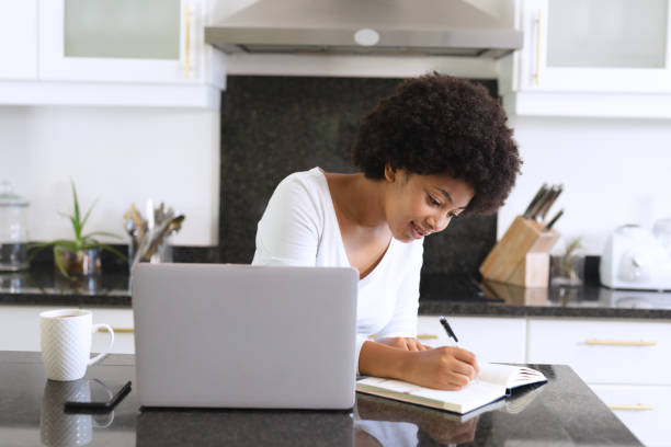 istock African american woman sitting in kitchen using laptop and taking notes 1309808897