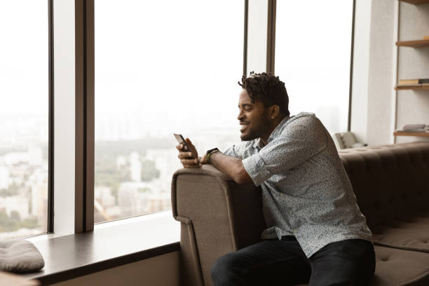istock Smiling African American man using phone, relaxing on couch 1309810182