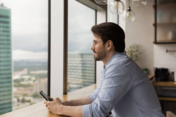 istock Side view dreamy man wearing glasses distracted from phone 1309812846