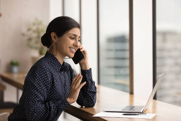 istock Close up smiling Indian woman talking on phone, using laptop 1309812877