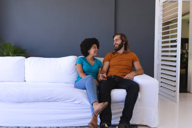istock Happy diverse couple sitting on sofa holding hands and smiling 1309813016