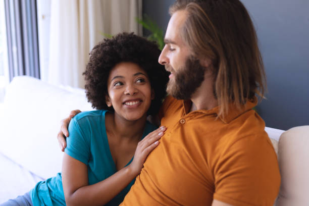 istock Happy diverse couple sitting on sofa embracing and smiling 1309813203
