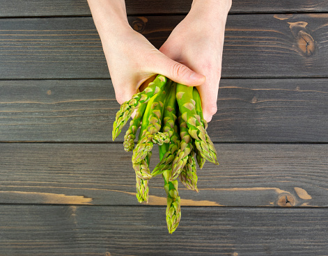 Hands hold a bunch of fresh asparagus over a black wooden table.