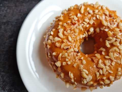 Delicious pastries. Donut covered with caramel and nuts on a white plate.