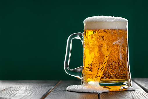 Beer is poured out of glass. Mug with traditional Irish ale on dark background. Place for text