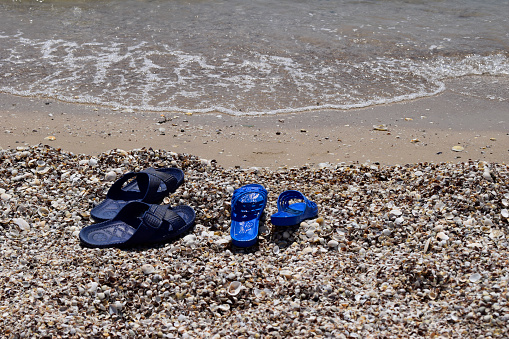 Summer slippers on the beach near the water. Sea shells on a sunny day. Tropical beach vacation and travel concept