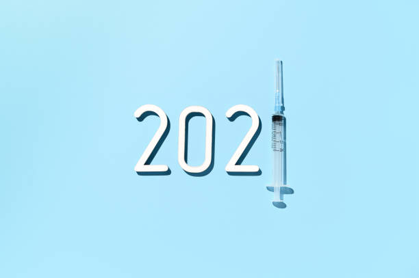 istock Overhead view of date 2021, syringe on pastel blue background 1309822626