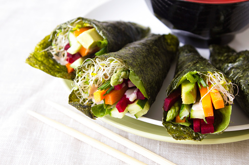 Healthy vegetable sushi wraps with raw vegetables and sprouts.
The wraps are made with seaweed nori sheets and dressed with a tahini dressing. 
Stock photo.