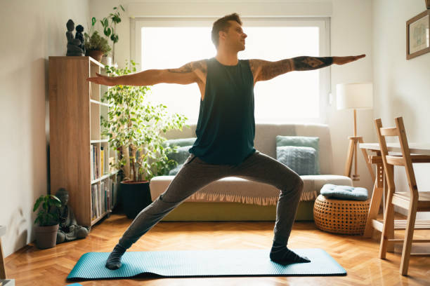 istock Young man practicing yoga at home and doing the warrior pose 1309835025