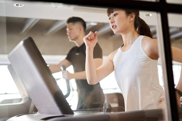 トレーニングジムでトレッドミルで走るアジアの女性 - フィットネスマシン ストックフォトと画像