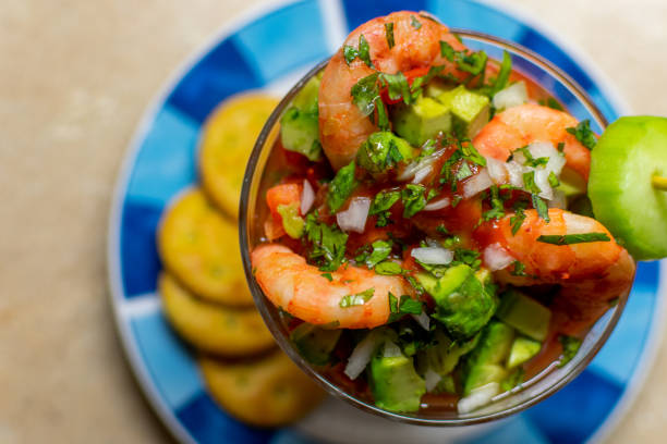 top view of a delicious shrimp cocktail with crackers, chopped onion, cilantro, avocado and lime, on a white plate with green. fresh mexican food - cocktail avocado imagens e fotografias de stock