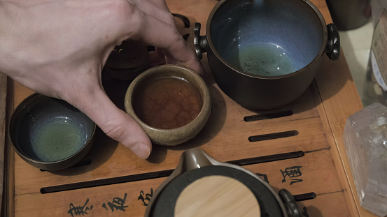 Tea board, camera shoots close up. Man hand picks up an earthenware cup of oolong tea. The concept of Chinese and Japanese tea ceremonies, hobbies and lifestyle