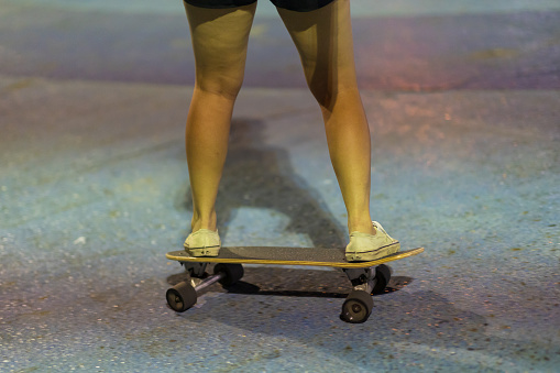 Close-up Asian women play surf skate or skates board outdoors at night.