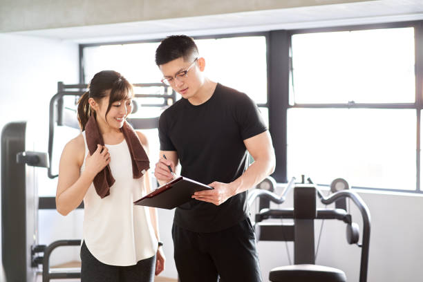 entrenador personal masculino asiático enseñando usando una tableta - gym machine smiling coach fotografías e imágenes de stock