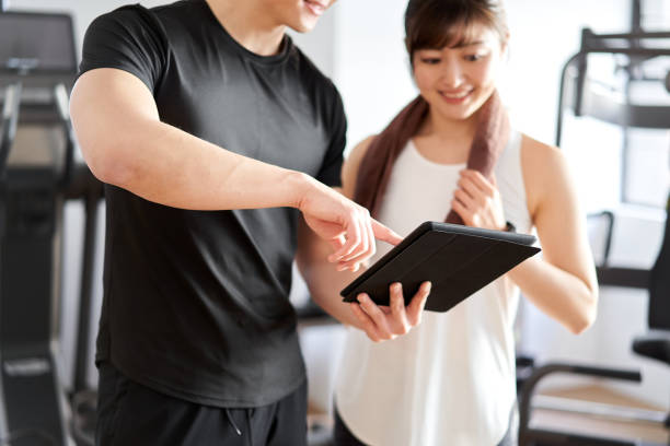 asiatische männliche personal trainer lehre mit einem tablet - japanese ethnicity train women asian ethnicity stock-fotos und bilder