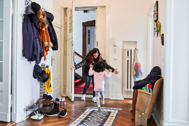 Girl Running Towards Happy Mother At Doorway Excited woman arriving home and reaching for daughter. Rear view of girl is running towards mother at doorway. They are in mudroom. reach destination stock pictures, royalty-free photos & images