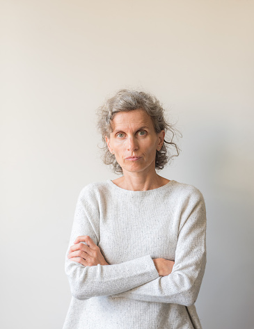 Waist up view of natural  middle aged woman looking frustrated with crossed arms against neutral wall background (selective focus)