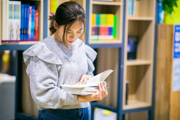 Young college girl reading book in library