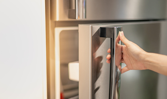 Mano femenina abriendo una puerta de refrigerador para encontrar la comida y el ingrediente que se preparan para cocinar en su hogar. photo
