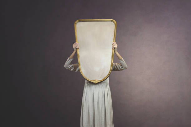 woman hides holding a mirror in front of her face; introspection concept - imagination fantasy invisible women imagens e fotografias de stock