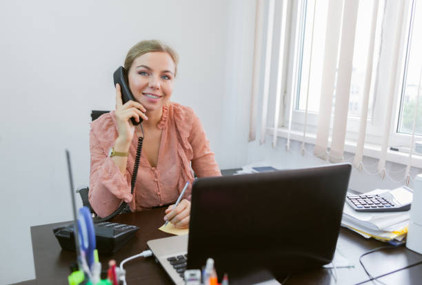 istock Everything is in work. Office worker woman talking on the phone and writing information on a piece of paper while sitting at the table with a laptop in the office 1309866903